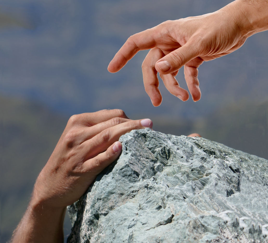 A hand grasping for another hand that is trying to climb a rock